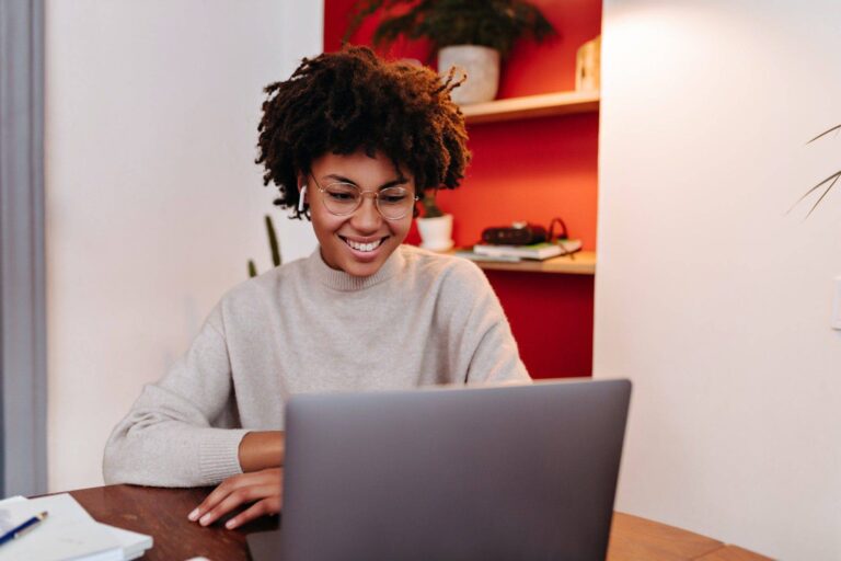woman in wireless headphones communicates via video link in laptop and posing in office with smile