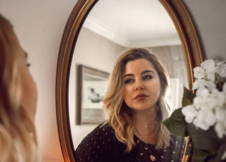 Liebe Frauen, weg mit dem Perfektionismus im Job! 3 Eine Frau blickt mit skeptischem Gesichtsausdruck in den Spiegel