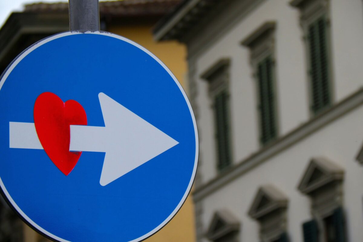 Gefühle am Arbeitsplatz: Das Bild zeigt ein rundest blaues Verkehrsschild mit einem weißen Pfeil. Darauf hat jemand ein rotes Herz gemalt, als ob der Pfeil durch das Herz geht.