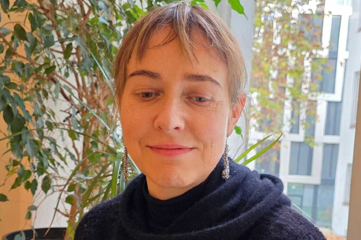 Beiträge 33 Porträt einer Frau mit kurzen Haaren und silbernen Ohrringen, sitzend vor einem Fenster mit Pflanzen im Hintergrund. Es handelt sich um Heike Sohna, die Geschäftsführerin von SEQUOYA.